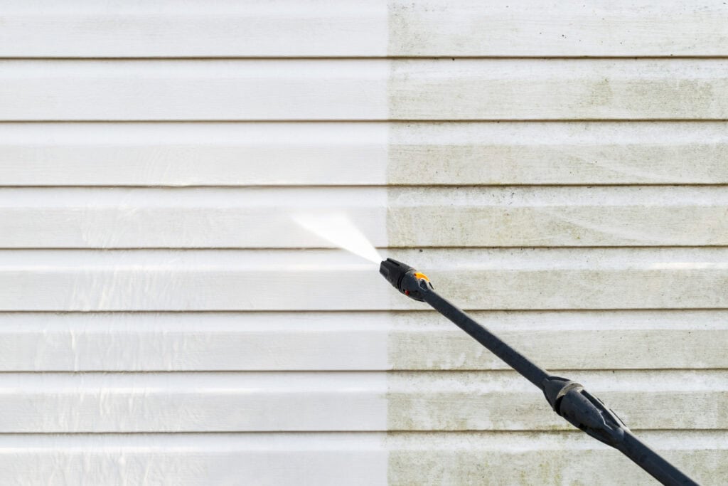 Pressure washing house siding to remove dirt and mold, preparing for painting or cleaning services.