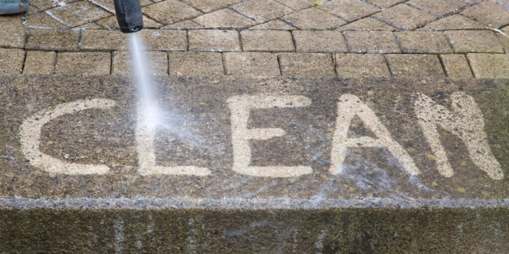 Clean pressure washing of concrete with "CLEAN" written in white chalk on pavement.