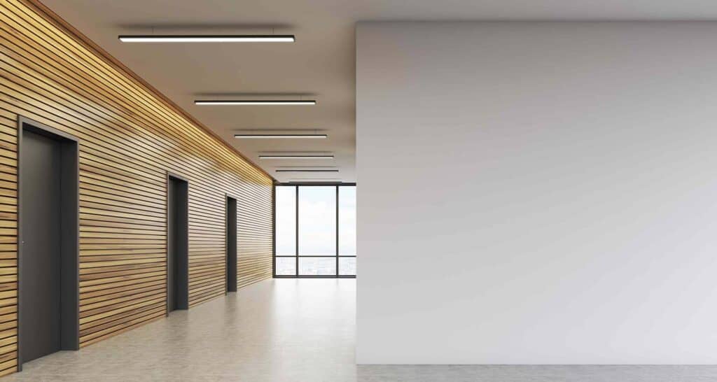 Modern elevator lobby with wood slat wall design and large window views, featuring sleek black elevator doors and bright lighting for a contemporary commercial space.