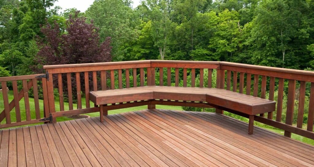 Rustic wooden deck with built-in bench overlooking lush green trees and vibrant foliage, perfect for outdoor relaxation and enjoying nature.