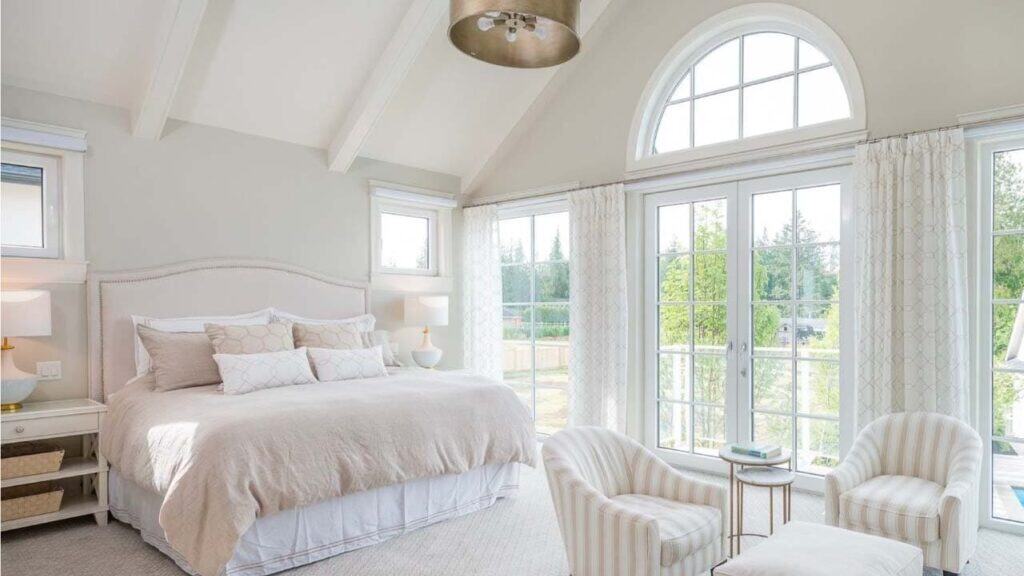 Bright bedroom with large arched window, neutral bedding, cozy armchairs, and soft natural light, showcasing professional interior painting and decoration by Thornapple Painting.